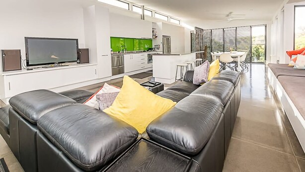 Een moderne woonkamer met een zwarte leren bank, een flatscreen-tv en een keuken met groene kastjes.