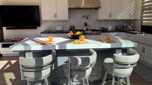 Une cuisine moderne avec des meubles blancs, un îlot central doté de tabourets et des luminaires suspendus.