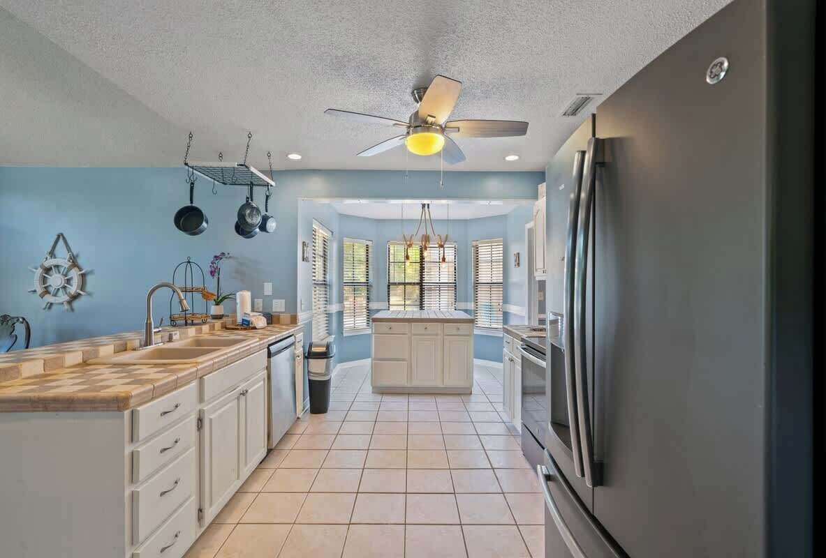 A kitchen with white cabinets, a central island, a ceiling fan, and a refrigerator.