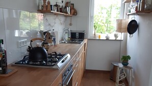 A modern kitchen with wooden cabinets, a gas stove, a sink, and a window with a view of greenery. - Apartment 'Ruhe Über Den Dächern Hannovers' with Private Terrace, Balcony and Wi-Fi (Hannover)