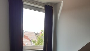 A bedroom with a bed, a window with curtains, a radiator, and a sloped ceiling. - Apartment 'Ruhe Über Den Dächern Hannovers' with Private Terrace, Balcony and Wi-Fi (Hannover)