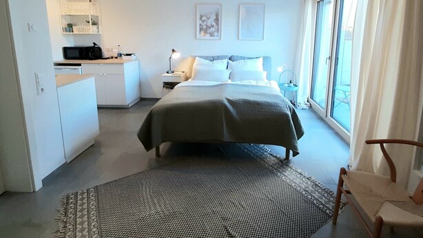 Quarto com cama, mesas de cabeceira, escrivaninha, cadeira, janela e vista para o exterior.