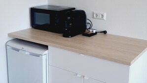 Uma cozinha compacta equipada com micro-ondas, mini-geladeira e um armário de vidro sobre o balcão.