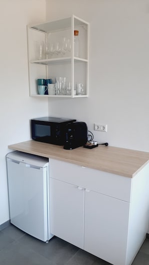A compact kitchenette with a microwave, a small refrigerator, and a glass cabinet above the counter.
