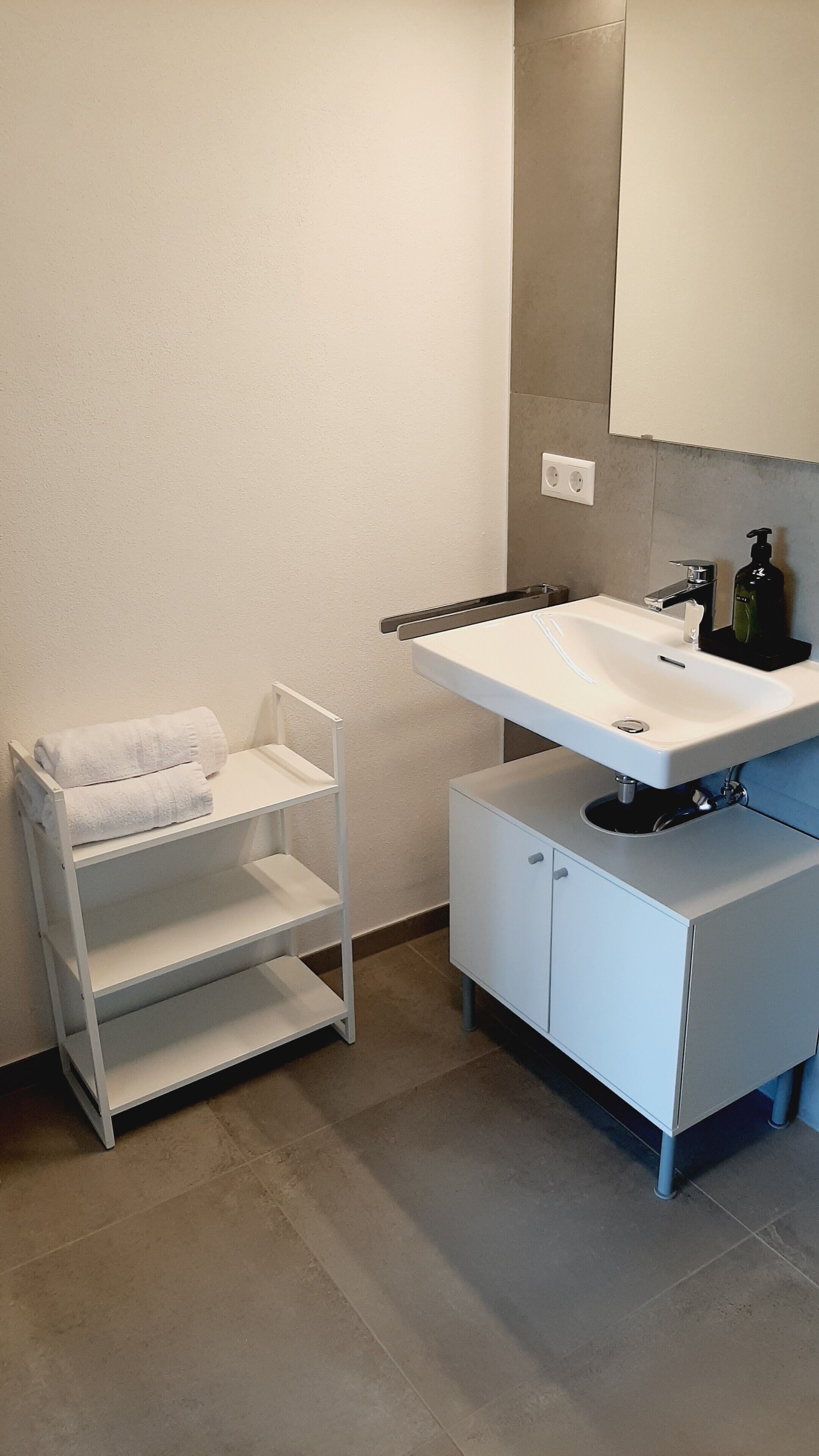 Un baño con lavamanos blanco, espejo, toallero y armario.