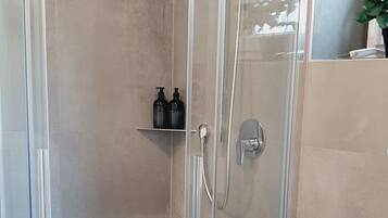 A modern bathroom with a glass-enclosed shower, a white toilet, and a small shelf with toiletries.