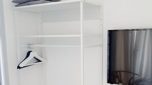 Quarto branco com armário embutido, um tapete preto na base e televisão na parede.