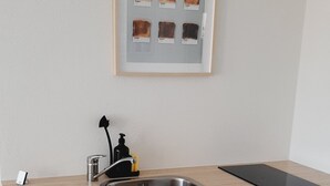 Cozinha com pia de aço inoxidável, bancada preta e quadro com uma fatia de pão torrado.