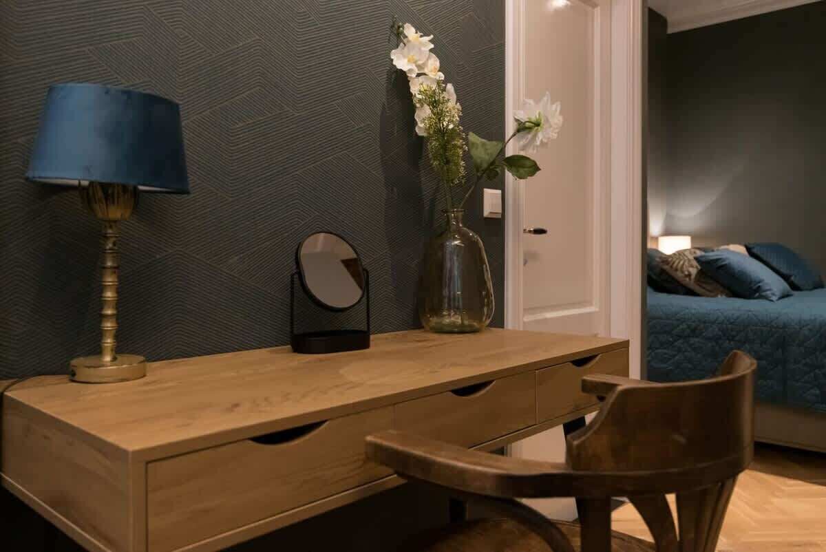 Een houten bureau met een lamp, een vaas met bloemen en een spiegel.