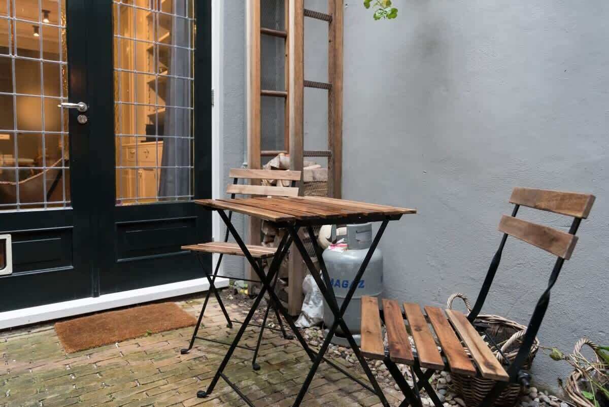A small outdoor seating area with a wooden table and chairs, a black door, and a gas cylinder in the background.