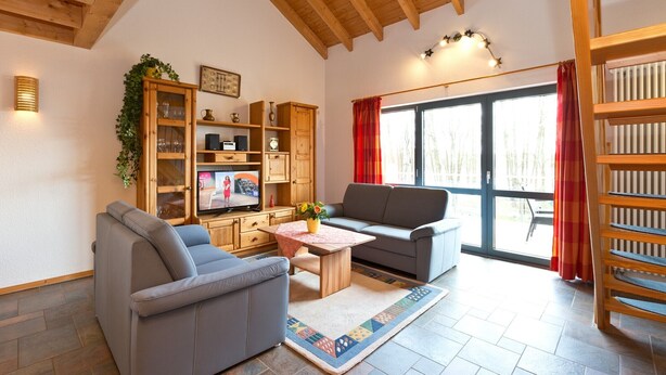 Ein Wohnzimmer mit einer Couch, einem Couchtisch, einem Fernseher, einem Holzschrank und einem großen Fenster mit Vorhängen.