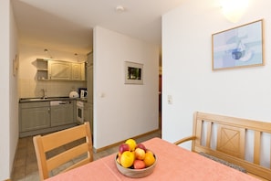A dining area with a table, chairs, and a fruit bowl. There is a kitchen in the background with cabinets and a sink. - Holiday Apartment 'Maribell' with Lake View, Balcony and Wi-Fi (Jabel)