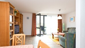 A living room with a sofa, a TV, a wooden cabinet, and a dining area. - Holiday Apartment 'Maribell' with Lake View, Balcony and Wi-Fi (Jabel)