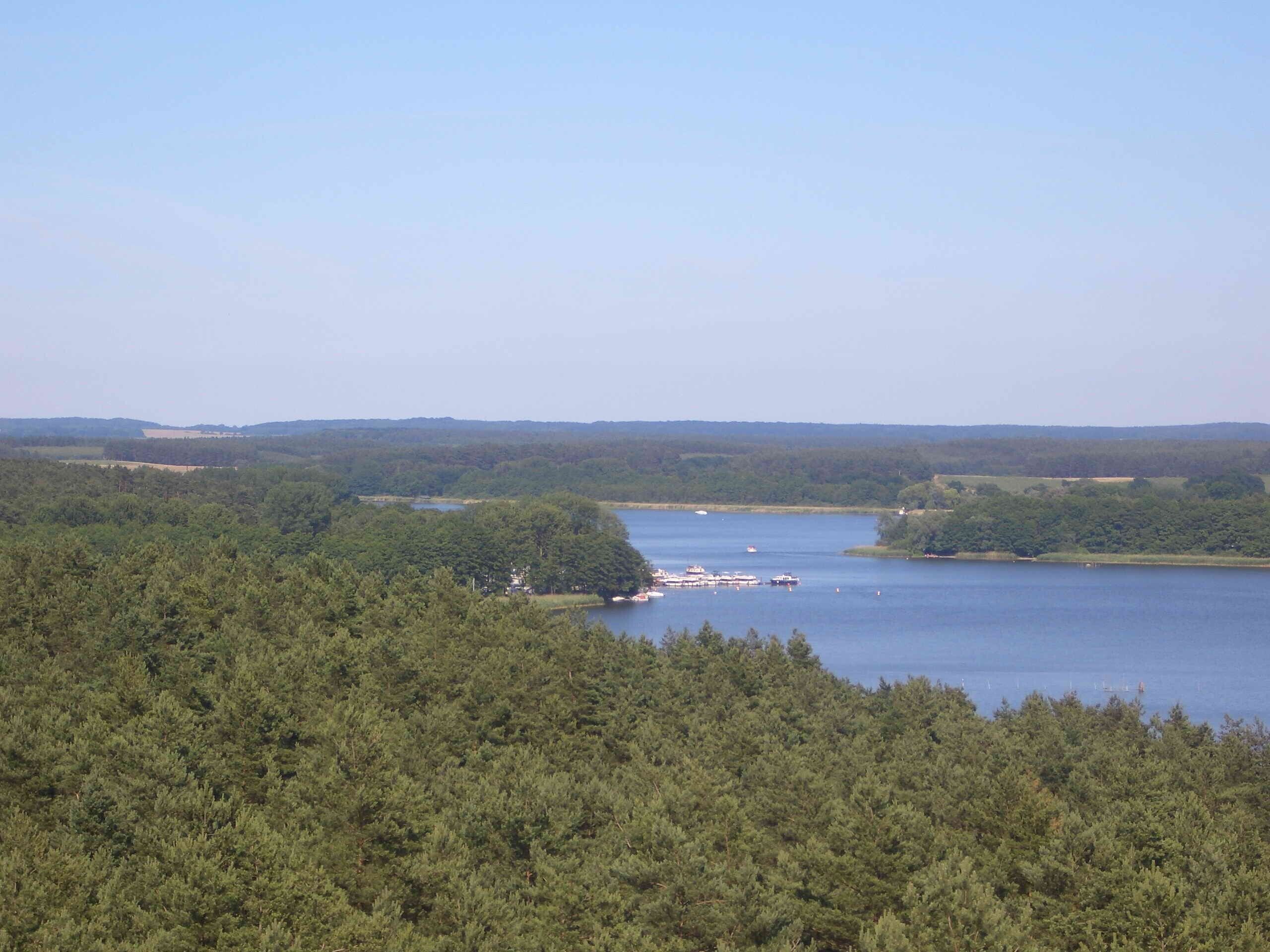 Un lac entouré d’une forêt dense, des bateaux sur l’eau et des collines à l’horizon.