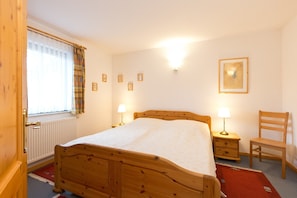A bedroom with a wooden bed, a chair, a nightstand with a lamp, and a window with curtains. - Holiday Apartment 'Maribell' with Lake View, Balcony and Wi-Fi (Jabel)