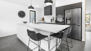 Een moderne keuken met een groot eiland, zwarte barkrukken, een koelkast en een waterdispenser.