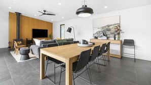 Een moderne woonkamer met een houten eettafel, zwarte stoelen, een open haard en een groot schilderij aan de muur.