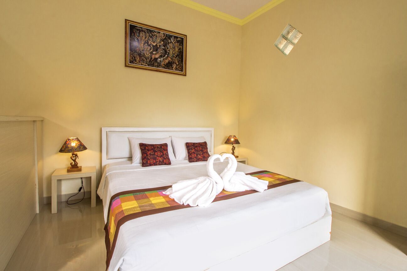 A hotel room with a large bed, two bedside lamps, a decorative painting, and a small window.
