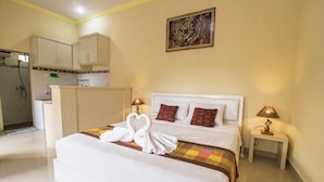 A hotel room with a bed, two bedside lamps, a nightstand, a bathroom with a shower, and a kitchen area. - Win House Ubud by Supala (Ubud)