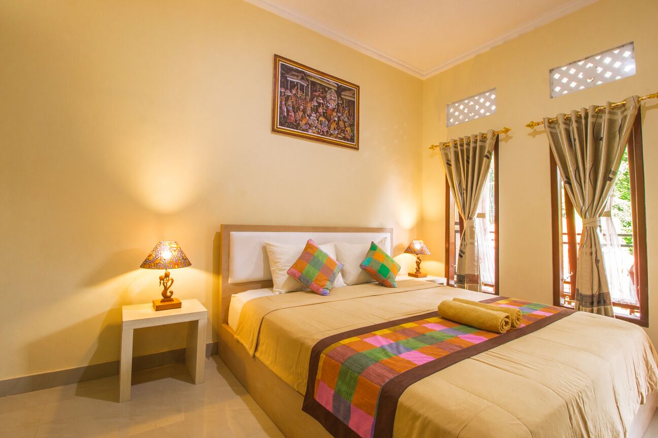 A hotel room with a large bed, two bedside tables with lamps, a colorful quilt, and a framed picture on the wall.