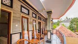 A balcony with wooden chairs and tables, framed artwork on the walls, and a view of a tiled roof and palm trees. - Win House Ubud by Supala (Ubud)