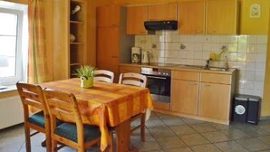 Une cuisine avec des meubles de rangement en bois, une table à manger avec des chaises, une machine à café et une poubelle.
