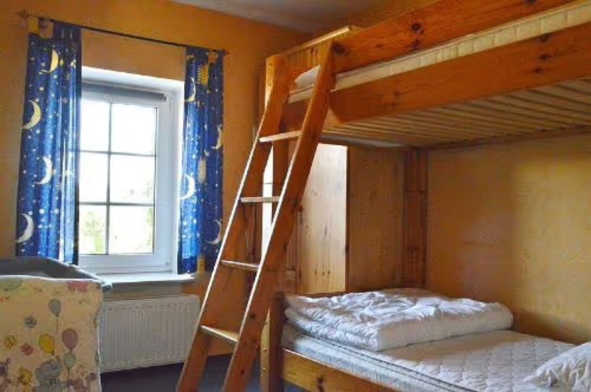 Een slaapkamer met een stapelbed, een houten trapje, een raam met gordijnen en een radiator.