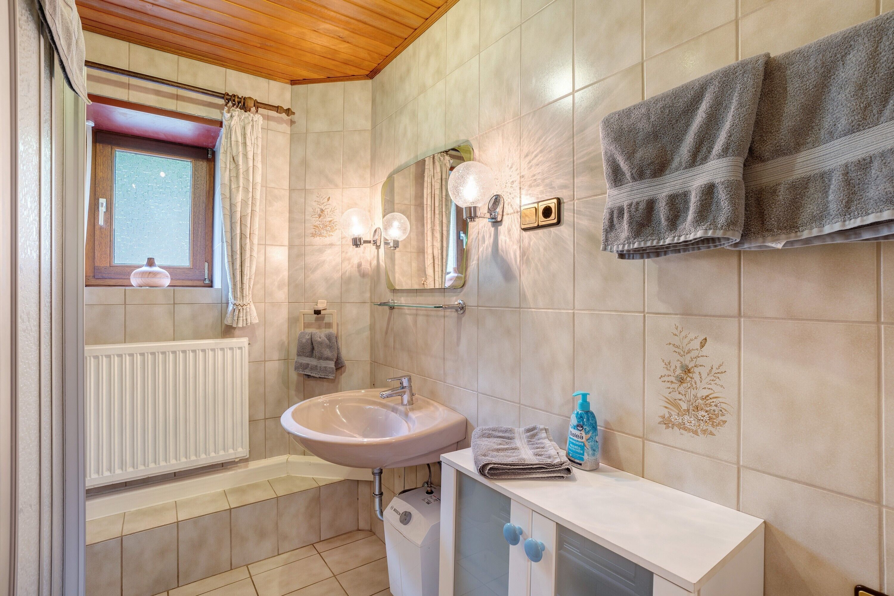 A bathroom with a sink, mirror, towel rack, and a window with a curtain.