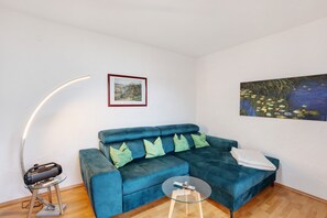 Ein Wohnzimmer mit einem blauen Sofa, einem Glastisch, einer Stehlampe und zwei Bildern an der Wand.