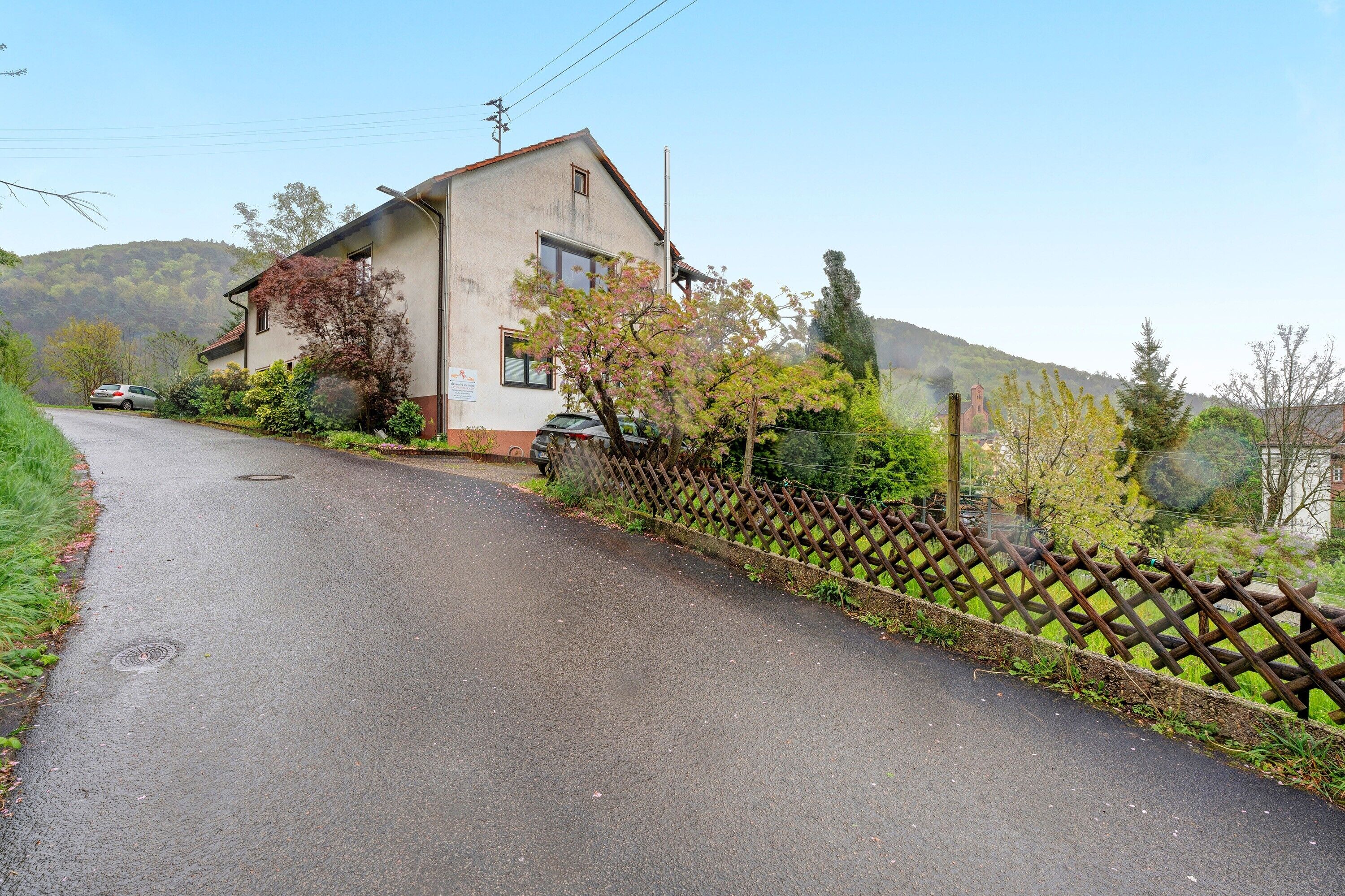 Une rue résidentielle avec une maison, une clôture et une voiture garée sur le bord.