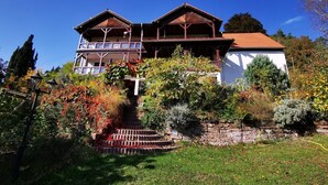 Un bâtiment à deux étages doté d’un balcon, entouré d’un jardin où poussent différentes espèces de plantes et bordé d’un mur en pierre.
