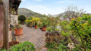 Un chemin pavé bordé de plantes en pot, une structure en bois et une vue sur un paysage vallonné.