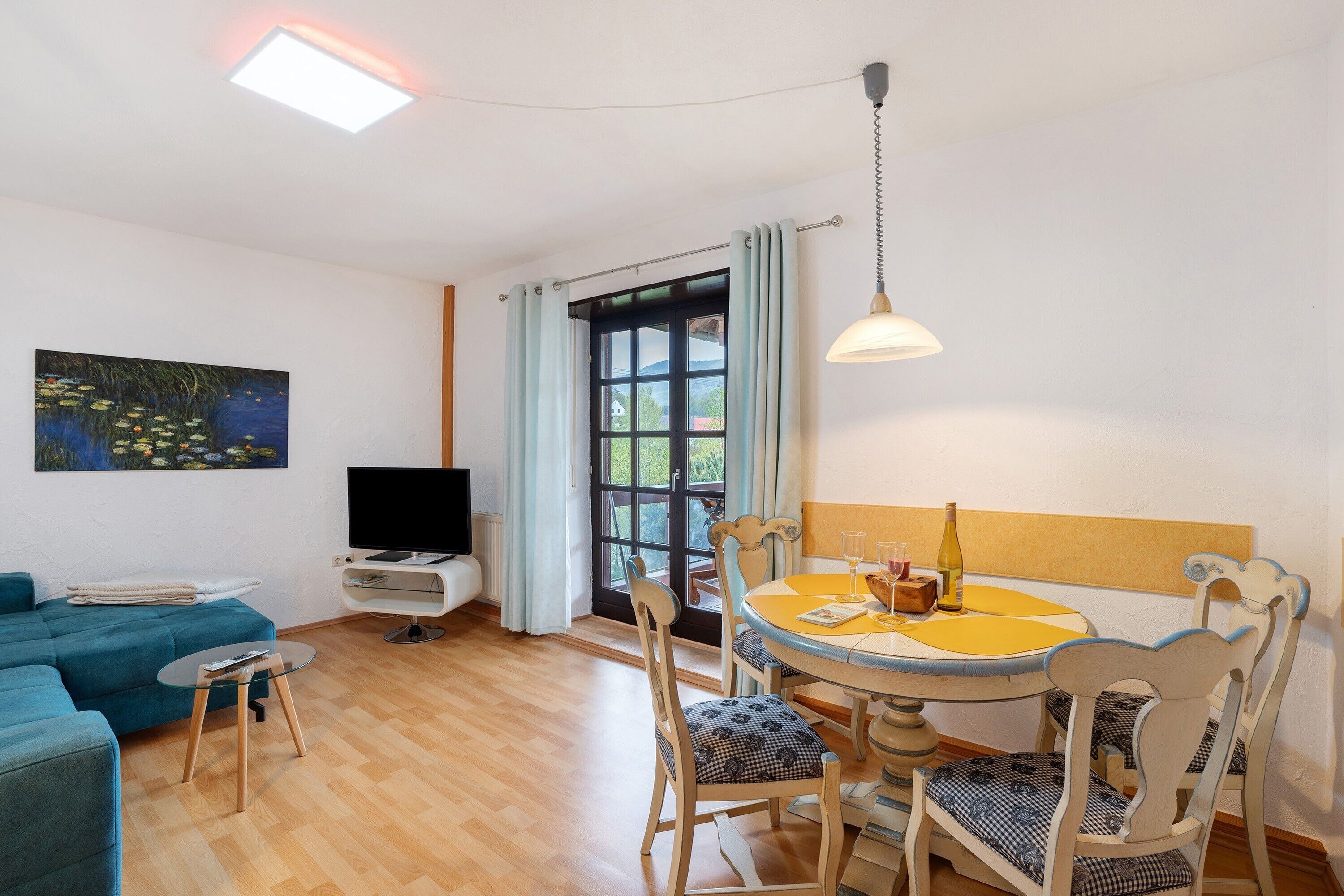 Una sala de estar con un sofá, una televisión, una mesa de comedor con sillas y un cuadro en la pared.