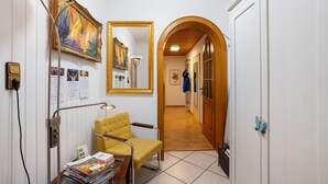 Un couloir avec une chaise jaune, une lampe, des œuvres d’art encadrées et une porte en bois.