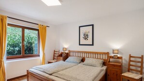 Une chambre à coucher avec un lit en bois, deux tables de chevet, une fenêtre avec des rideaux, un radiateur et un tableau encadré au mur.