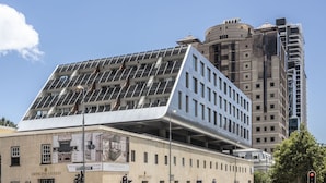 A modern building with a unique sloped roof design, featuring a large glass facade. - Studio Apartment With Balcony (Cape Town)