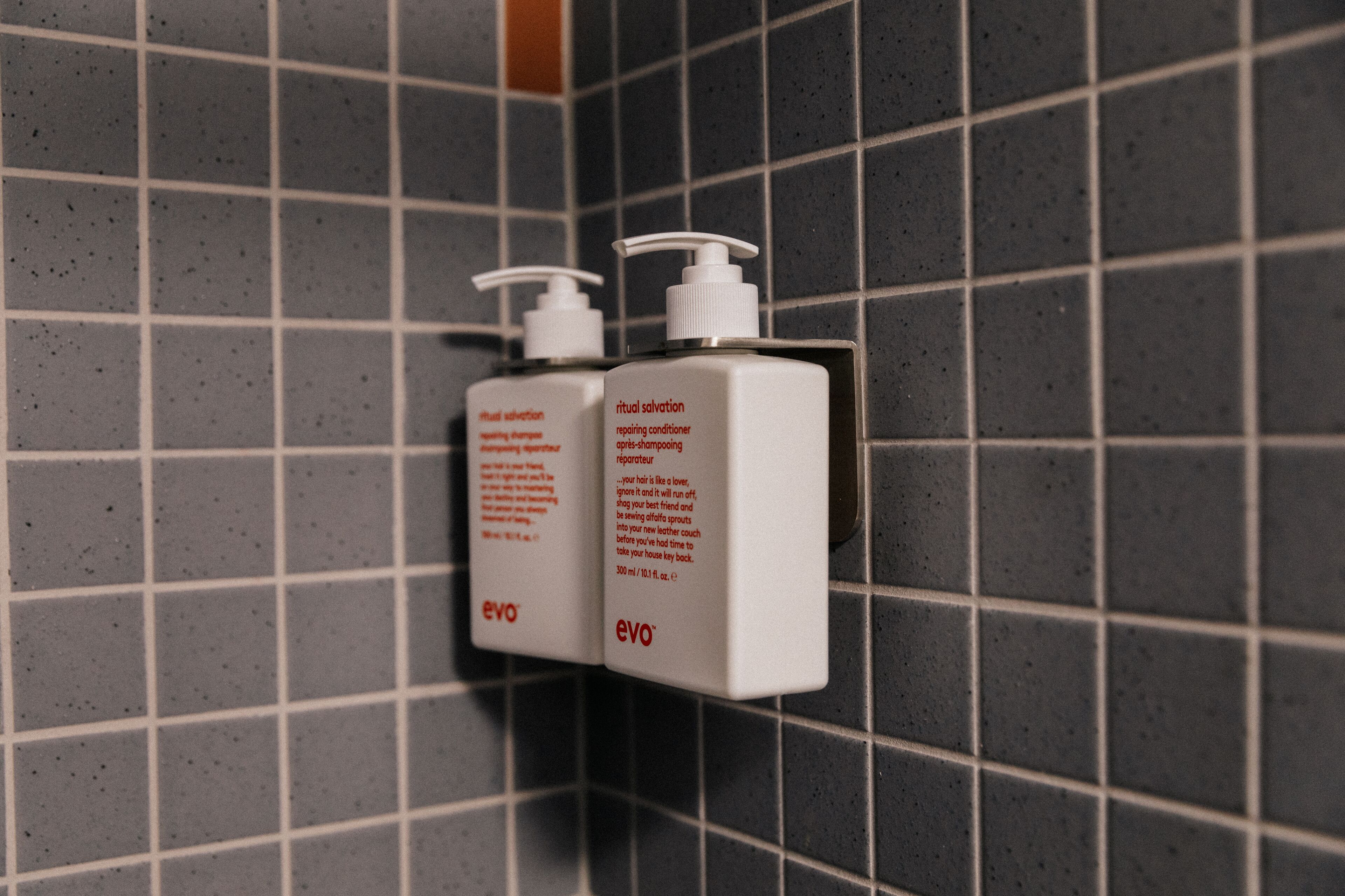 Two bottles of 'Evo' shampoo and conditioner on a tiled wall.