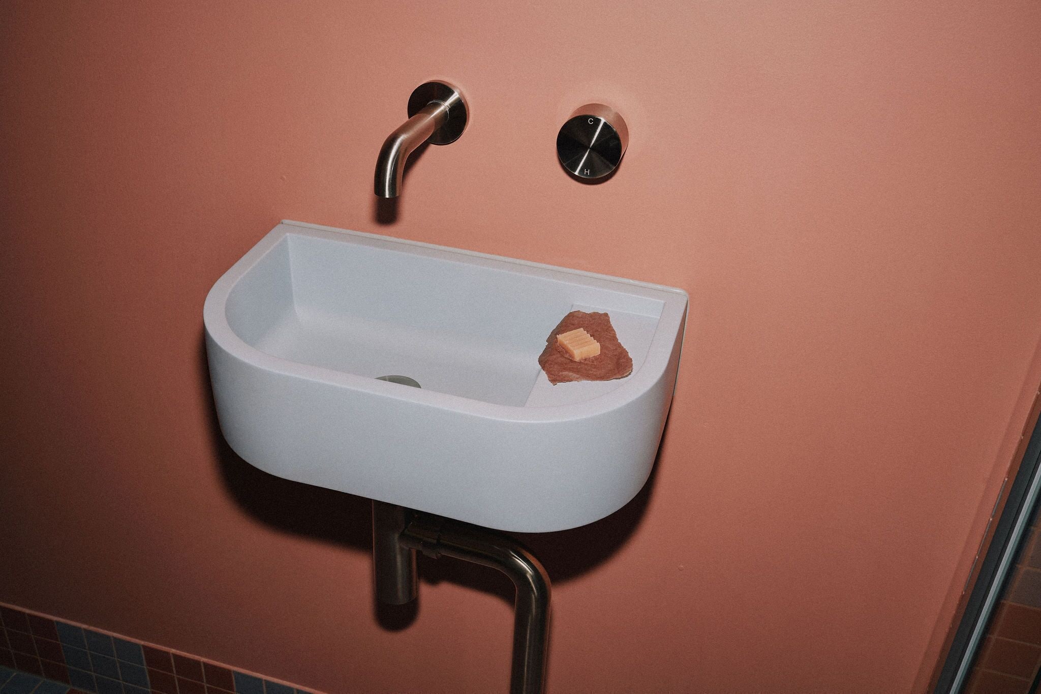 A white sink with a soap bar on the right side, mounted on a pink wall with a metal faucet and a round control knob.