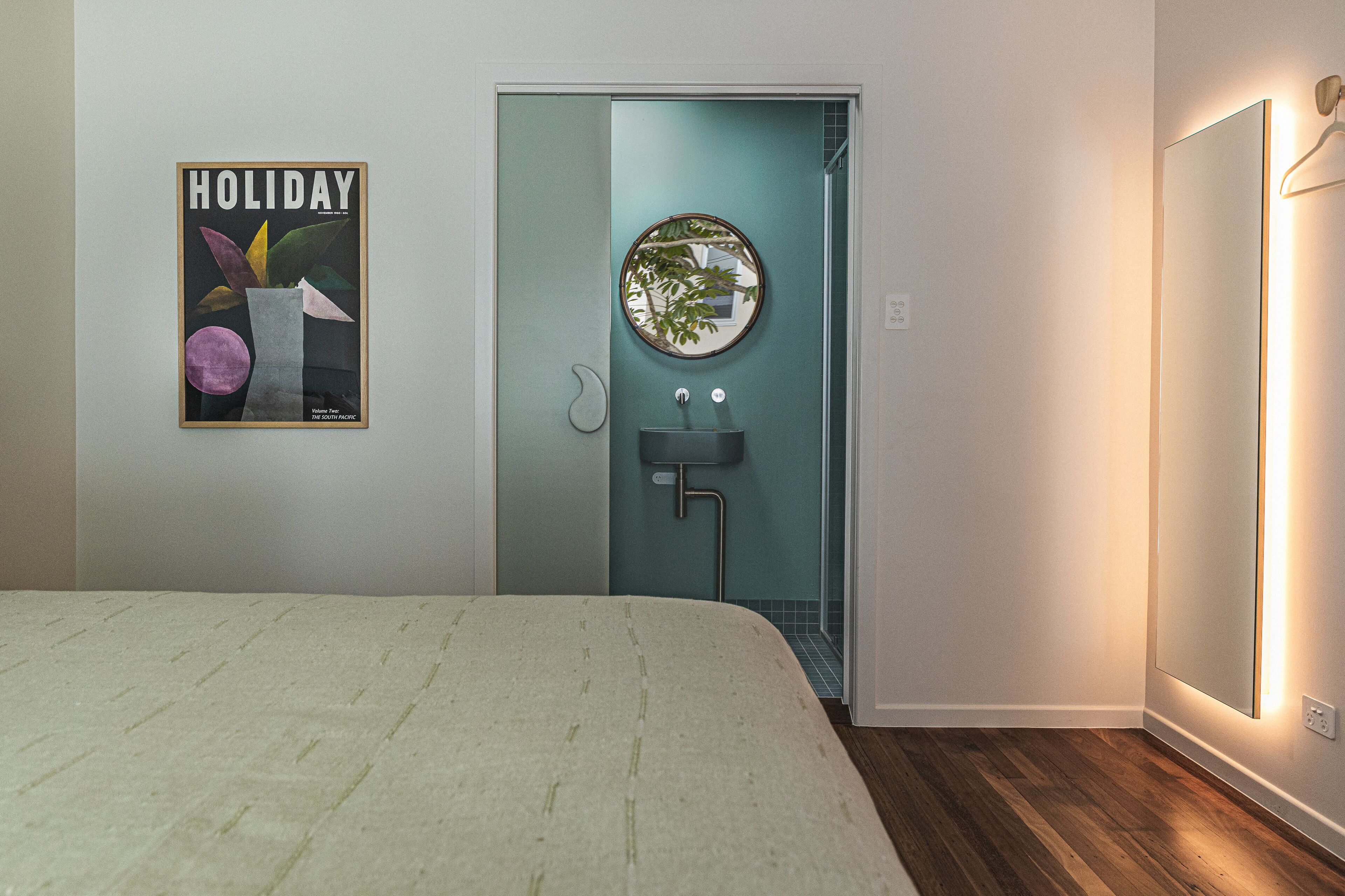 A bedroom with a bed, a bathroom with a sink and mirror, and a poster on the wall.