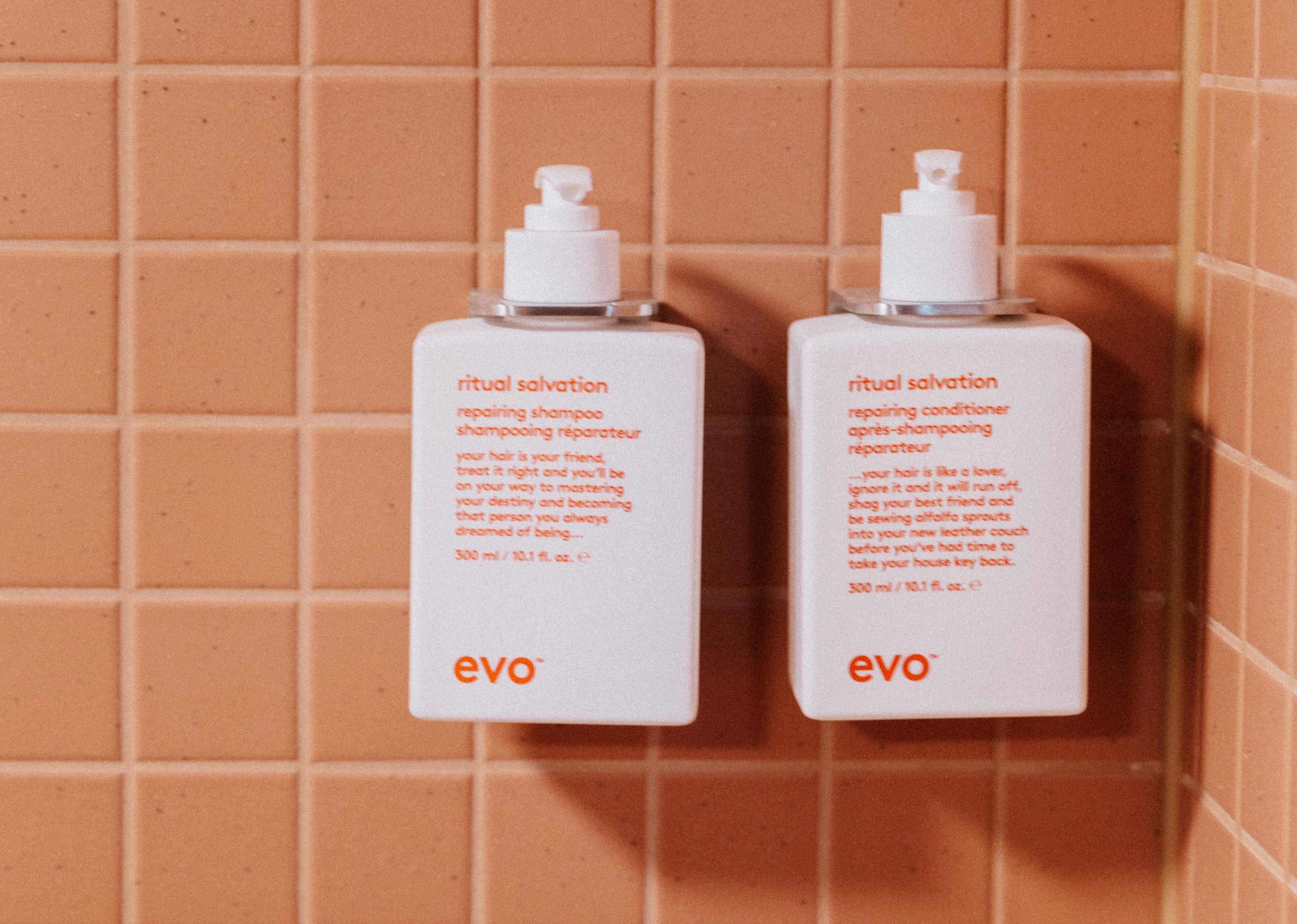 Two bottles of 'ritual salvation' shampoo and conditioner by 'evo' against a tiled wall.