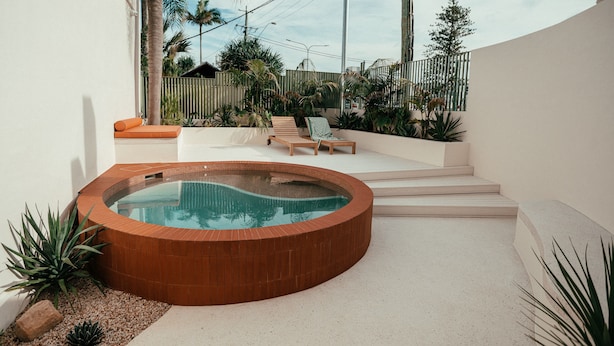 A circular hot tub with steps leading up to a seating area with two lounge chairs.