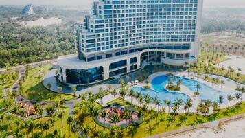 A modern hotel with a large pool area, surrounded by palm trees and greenery.