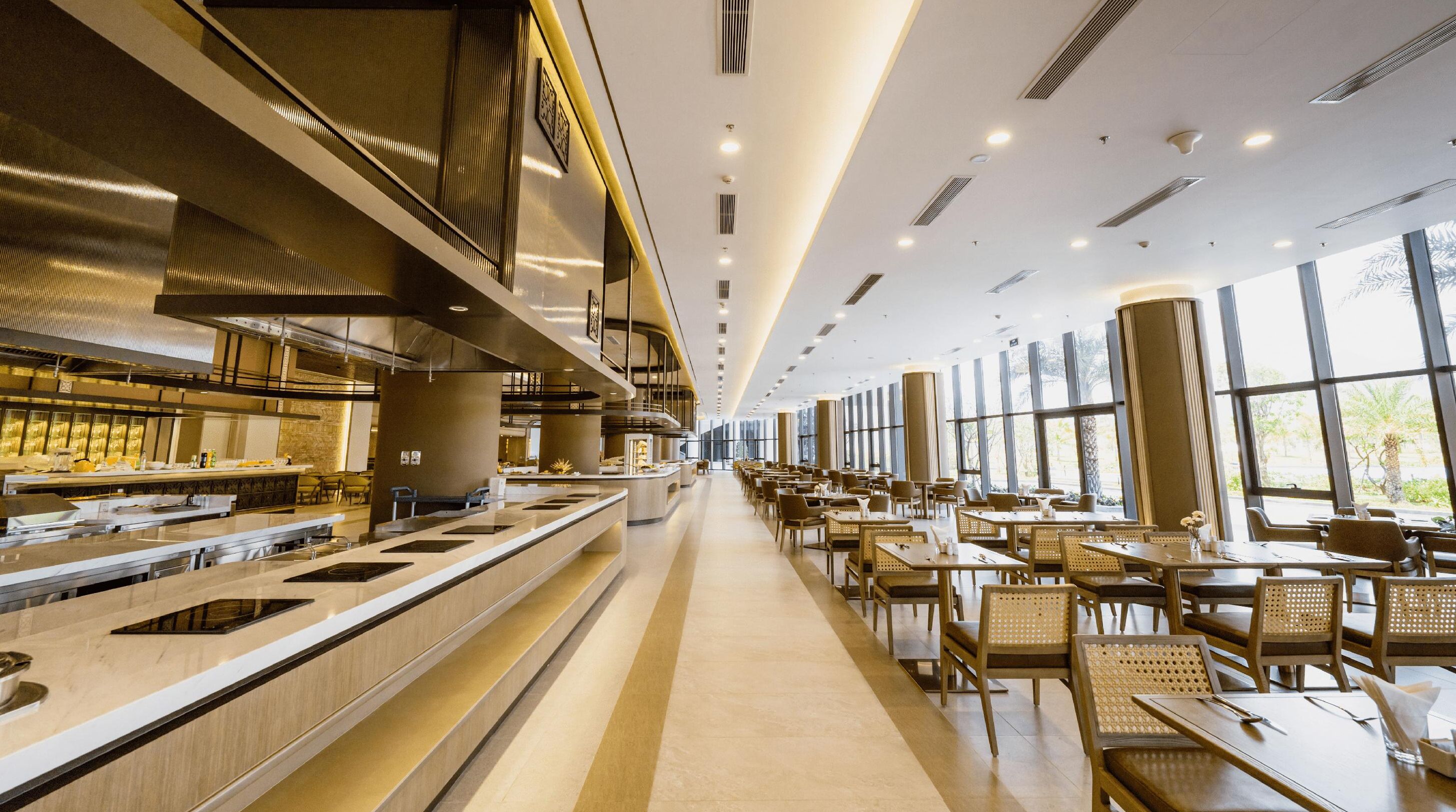 Un restaurante moderno con una barra larga, varias mesas y ventanas amplias que dejan entrar luz natural.