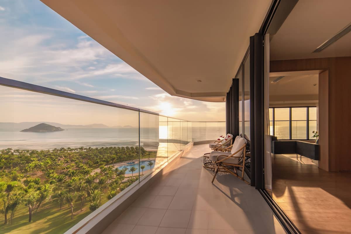 A balcony with a view of a beach and pool, furnished with chairs and a table.