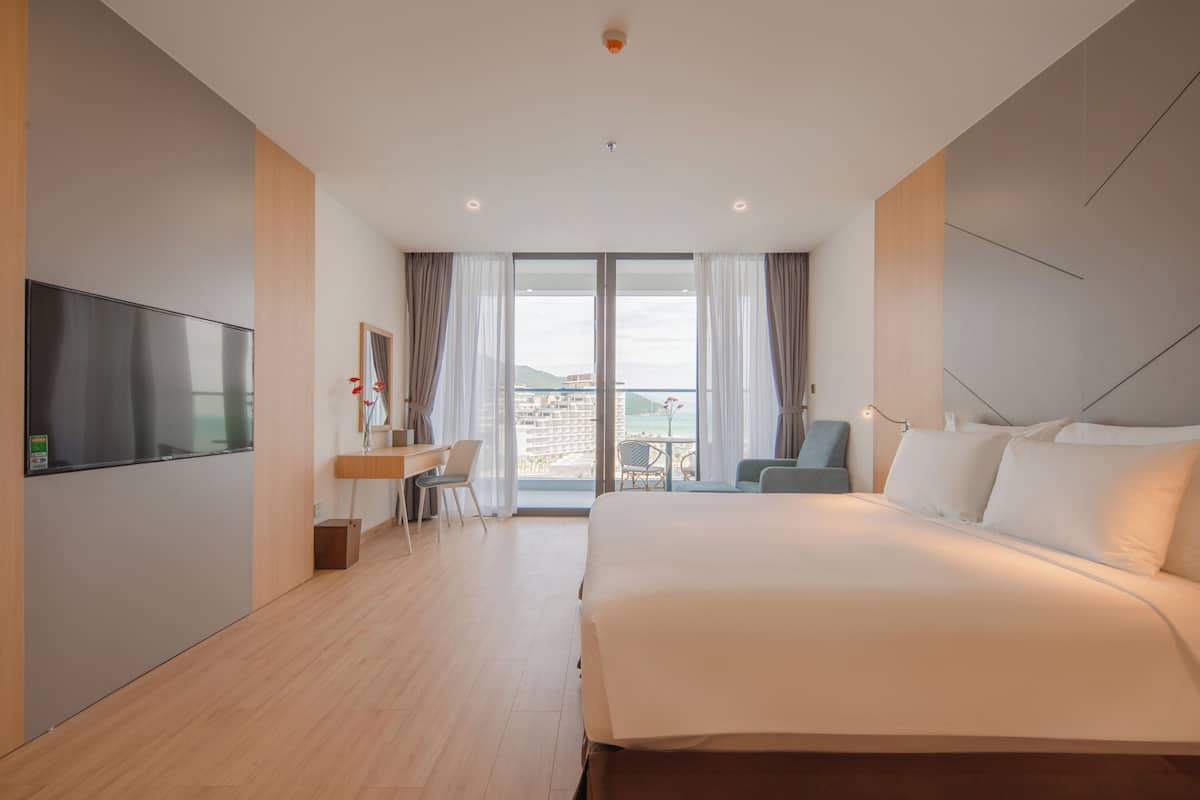 A hotel room with a bed, a desk, a chair, a TV, and a balcony with a view.