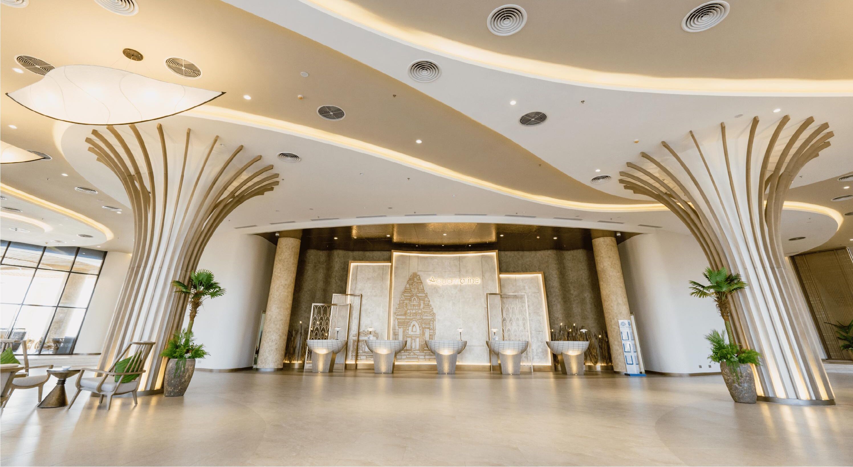 A spacious lobby with modern architecture, featuring a central seating area with chairs and tables, and large decorative columns.