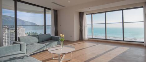 A modern living room with a grey sofa, a white coffee table, and a view of the sea and mountains.