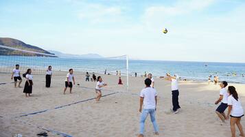 Partido de voleibol de playa en una cancha arenosa con red, rodeado de gente y el mar al fondo.