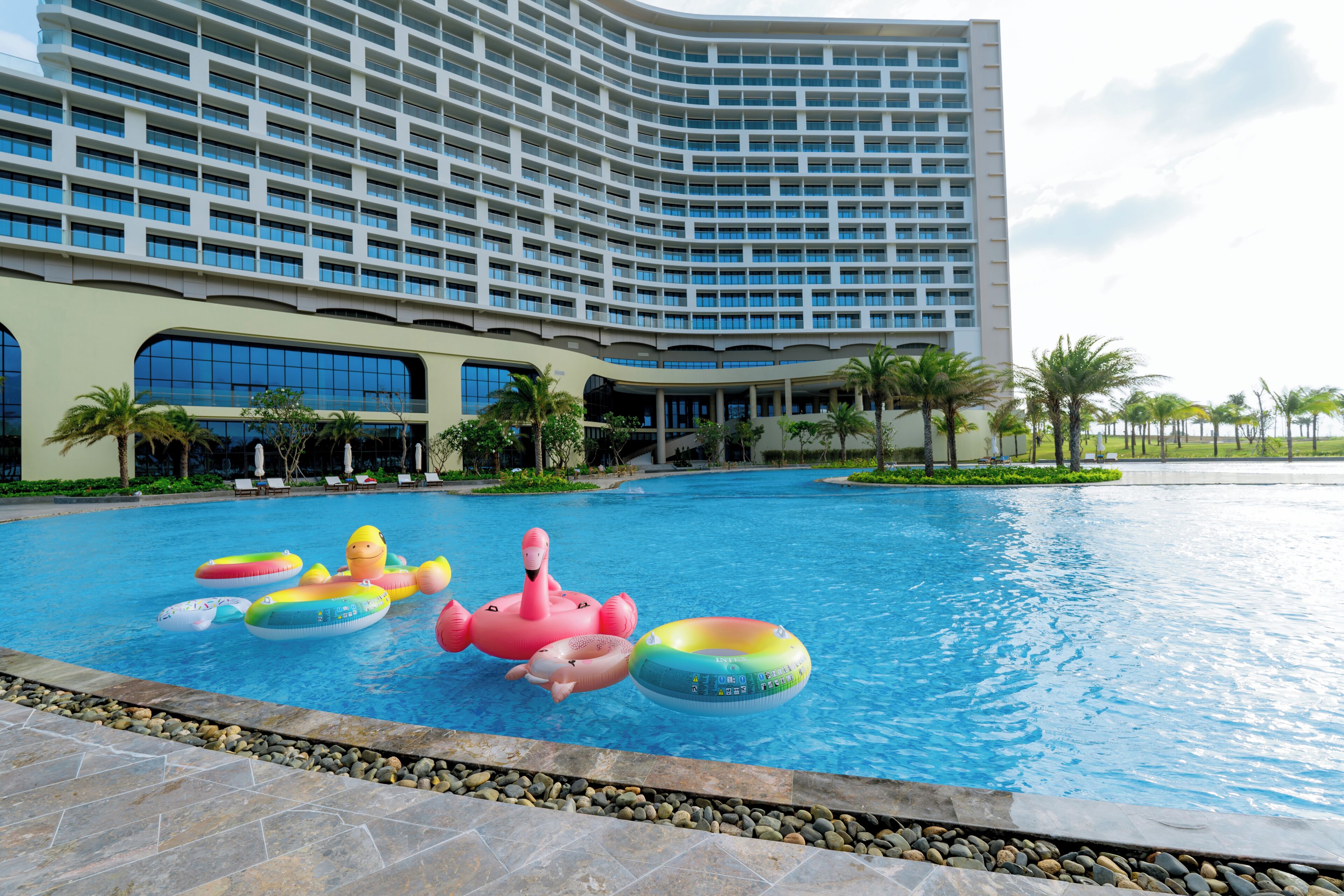 Una piscina con juguetes inflables y un hotel al fondo.