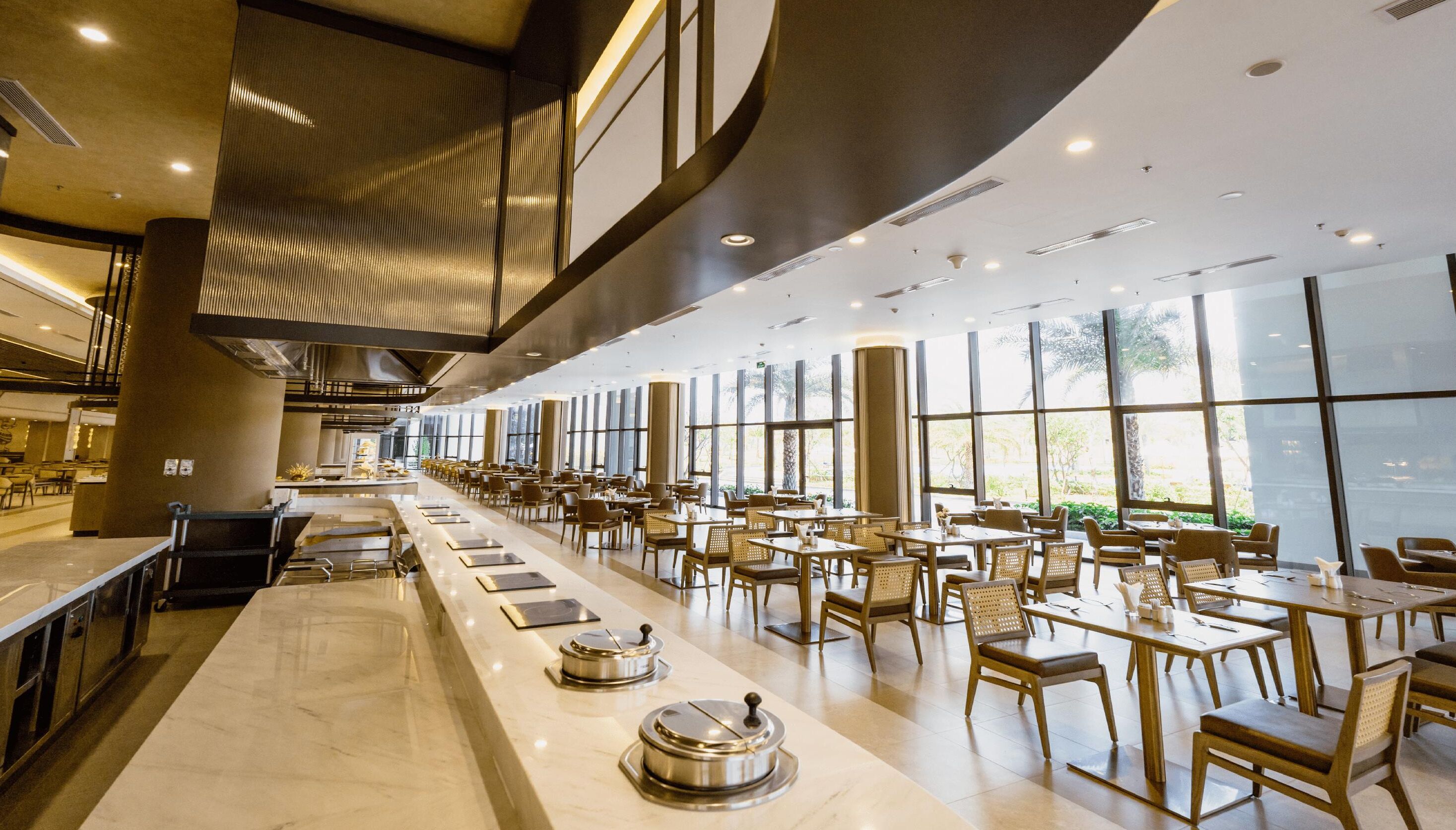 A spacious restaurant with high ceilings, large windows, and a long counter with tables and chairs.